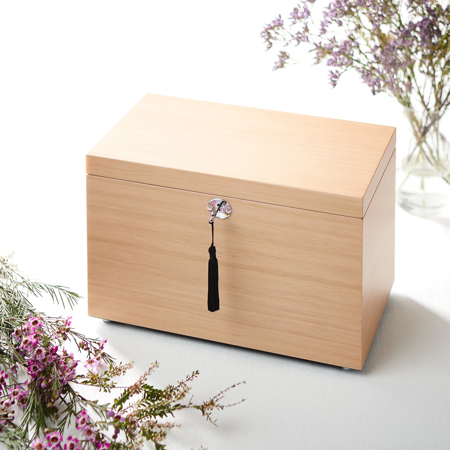 Wooden jewelry box with a decorative tassel on a white surface with flowers.