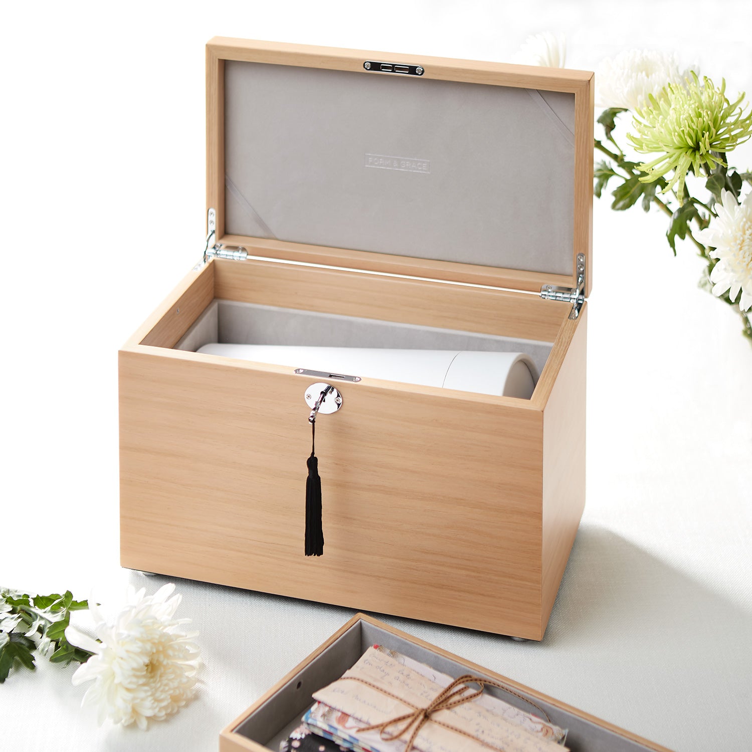 Wooden jewelry box with a tassel on a white surface with flowers.