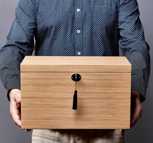 Person holding a wooden box with a black handle against a gray background