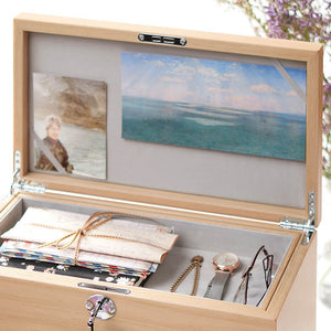 Wooden jewelry box with a lid featuring a painting of a beach scene, containing jewelry and stationery items.