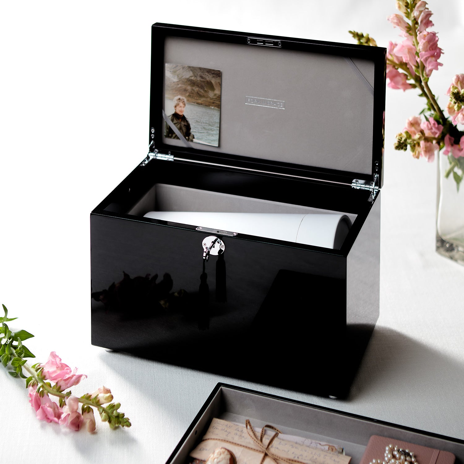Black jewelry box with a mirror on a white surface with flowers.