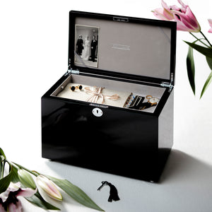 Black jewelry box with jewelry inside on a white surface with flowers.