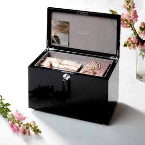 Black jewelry box with jewelry items on a white surface with flowers.