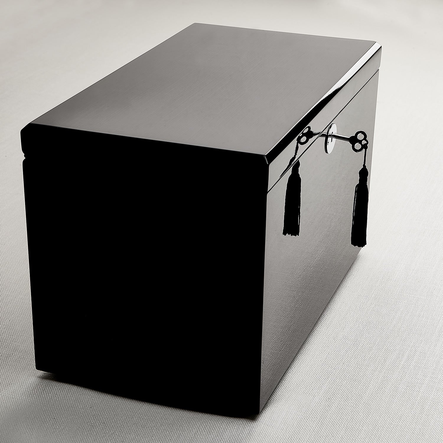 Black rectangular box with decorative tassels on a light gray background