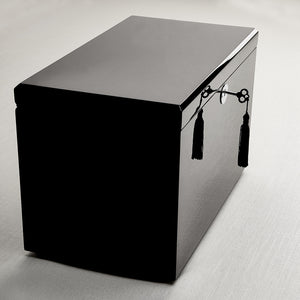 Black rectangular box with decorative tassels on a light gray background