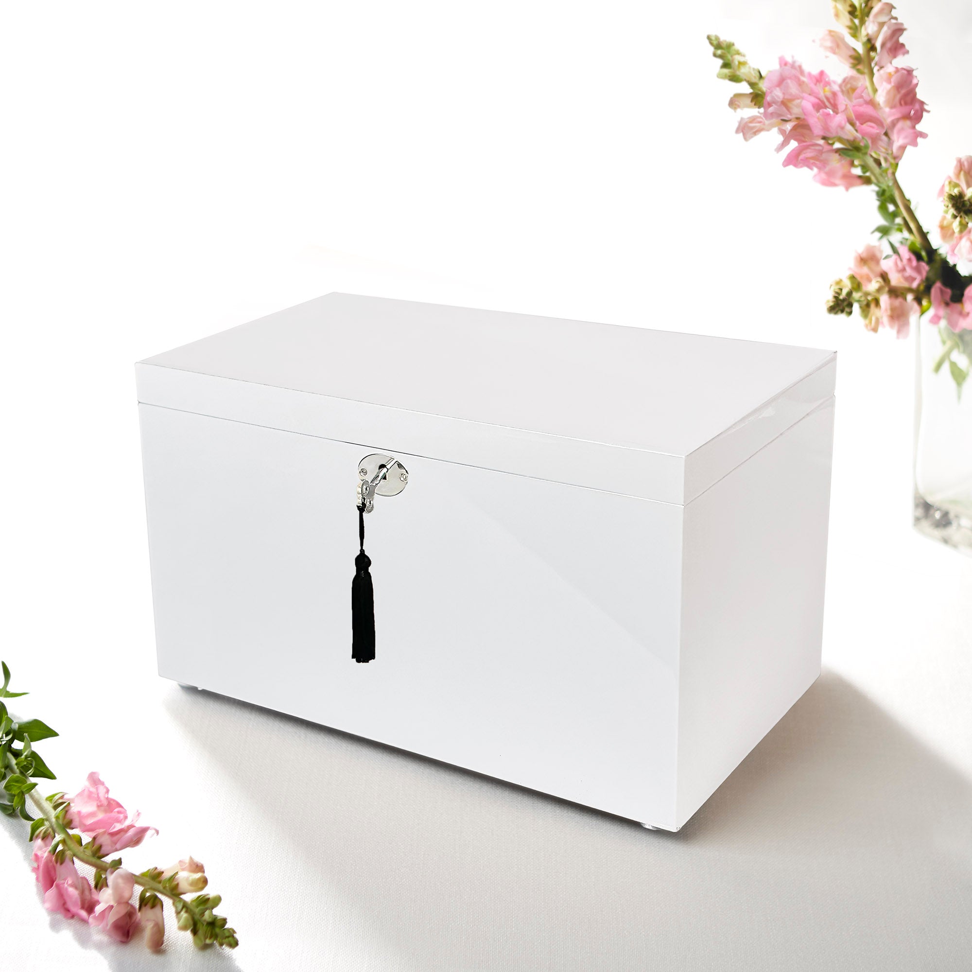 White jewelry box with a black tassel on a white surface with floral decorations.